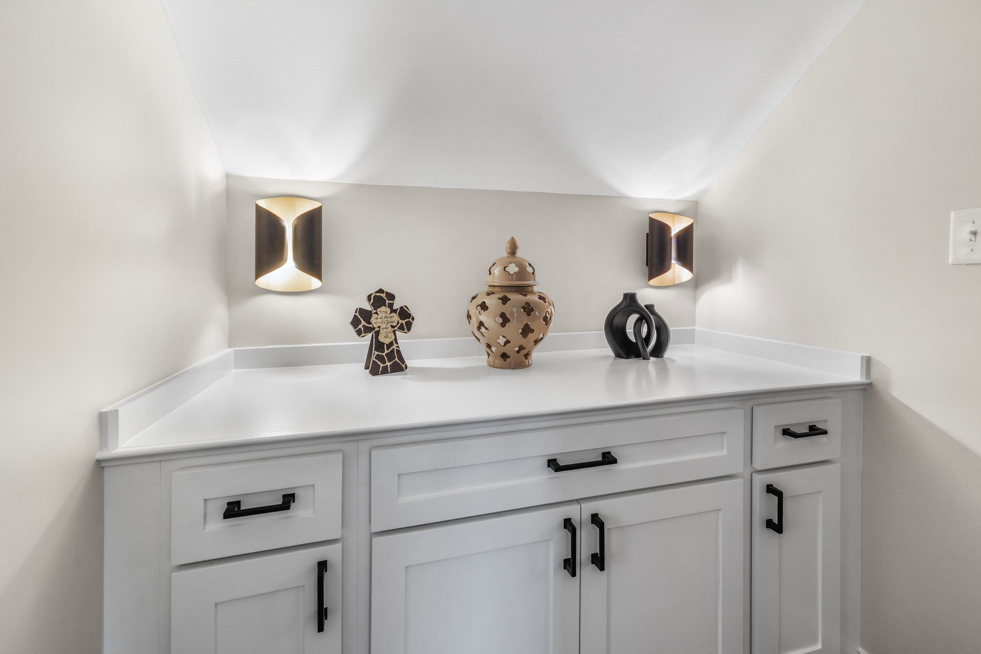 White cabinet with decor and sconces, set against a light-colored wall.