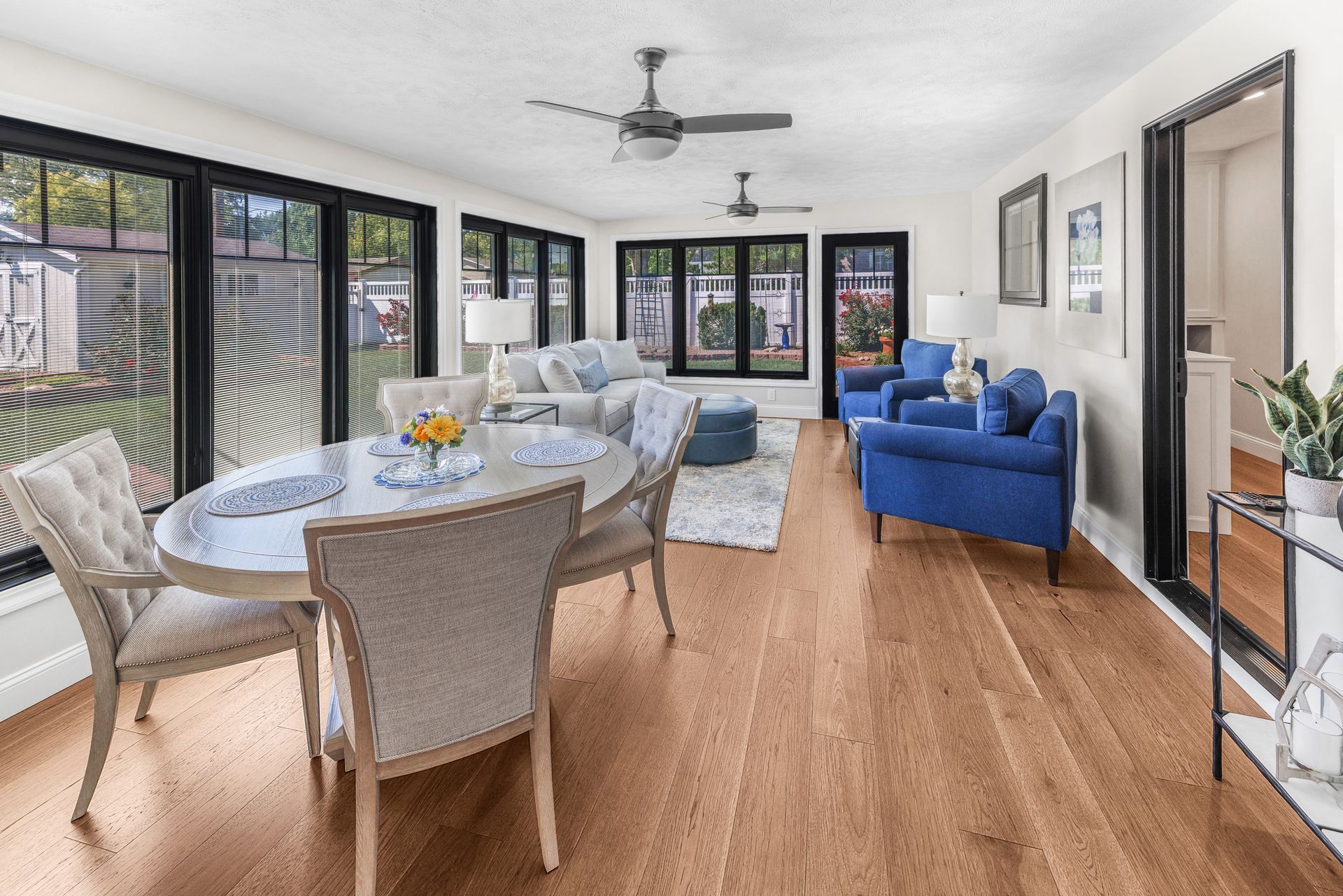 Bright sunroom with hardwood floors, dark window frames, and light-colored furniture.
