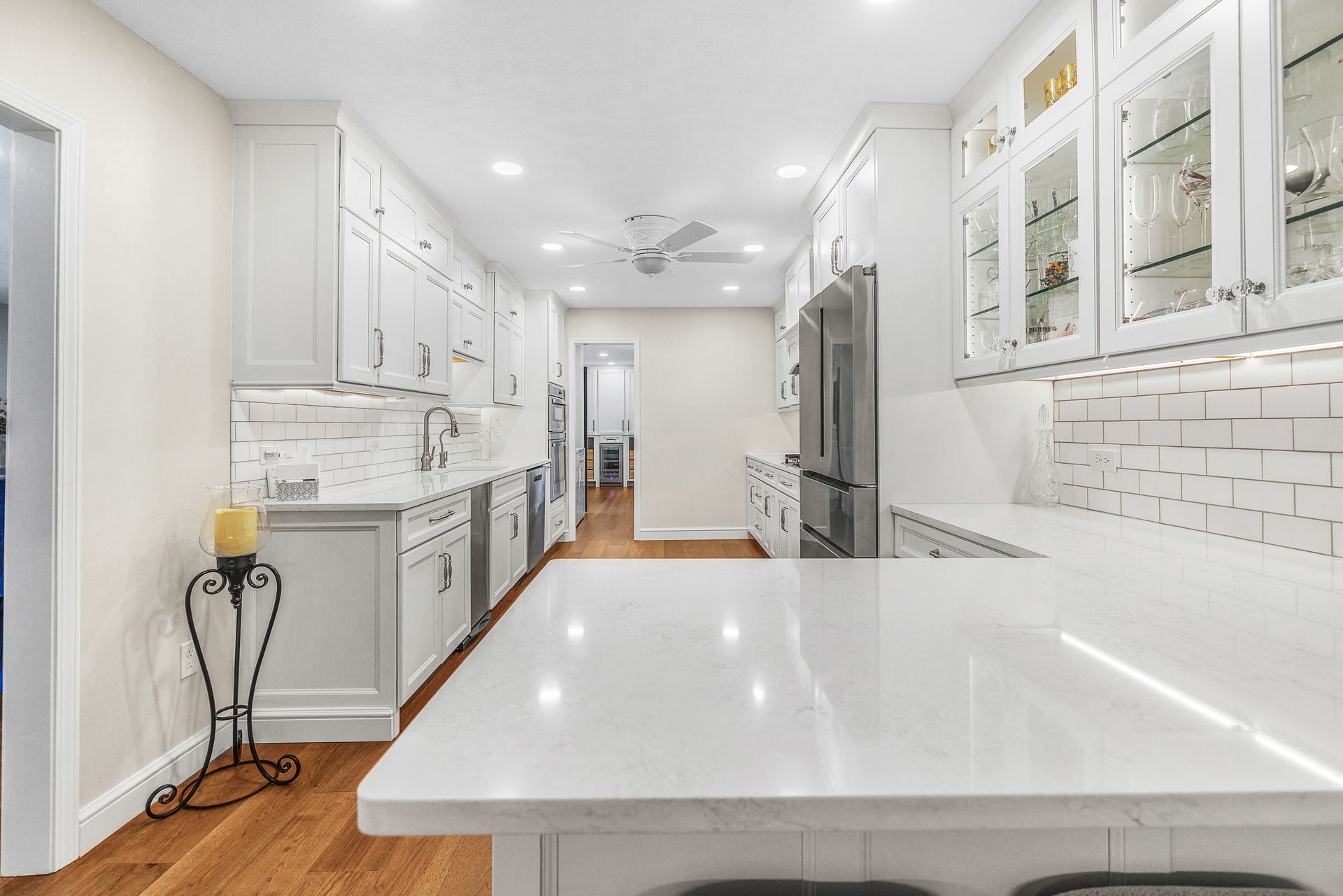White kitchen with long countertop, white cabinets, stainless steel appliances, and hardwood floors.