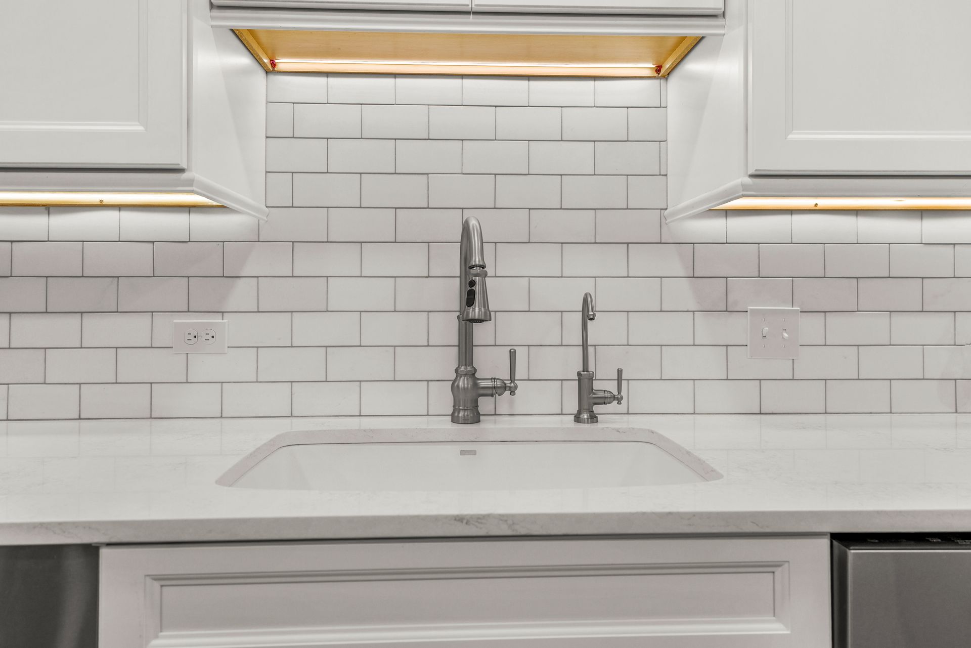 Kitchen sink with white cabinets, subway tile backsplash, and stainless steel faucet.