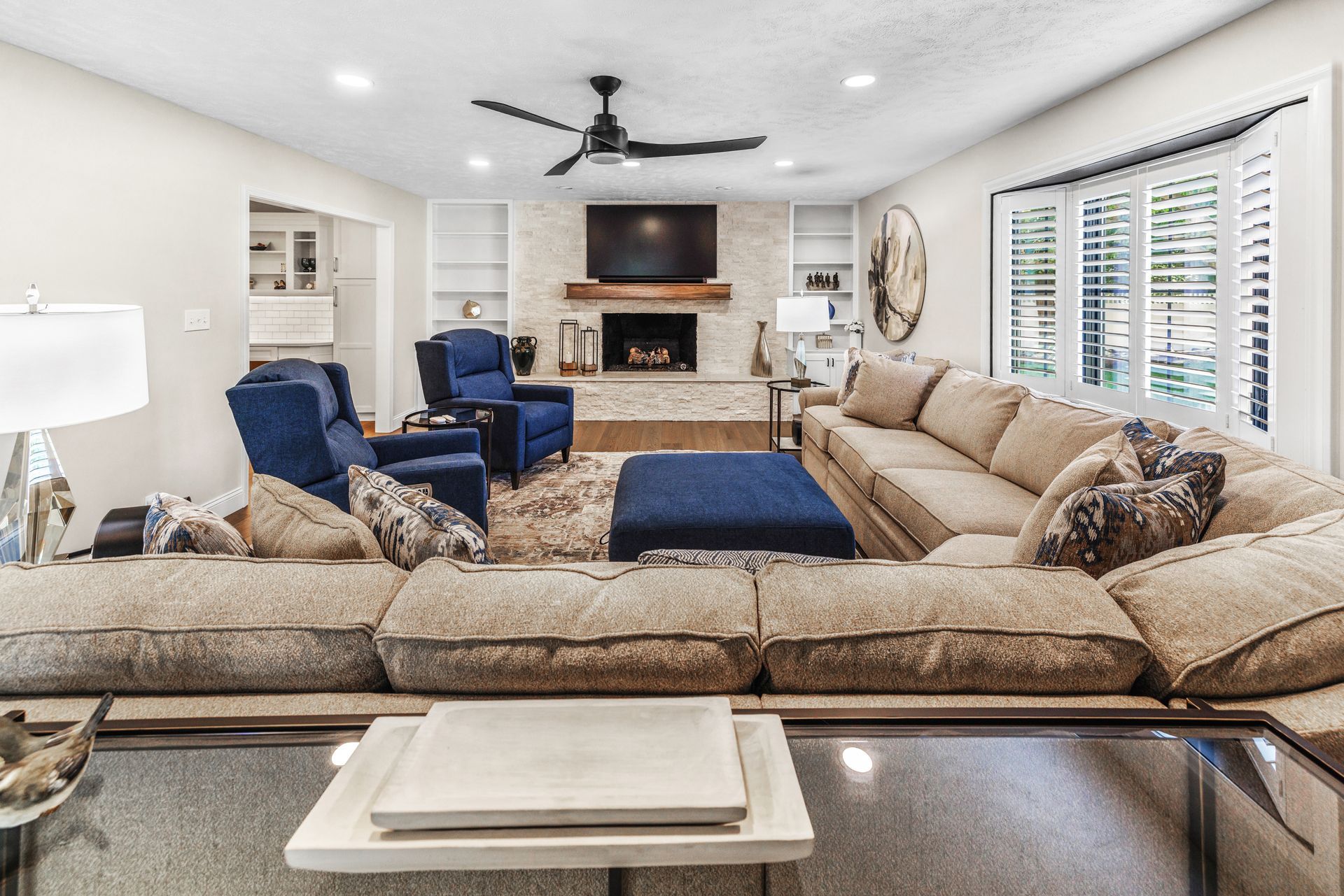 Living room with beige sectional, fireplace, blue chairs, and open shelving.