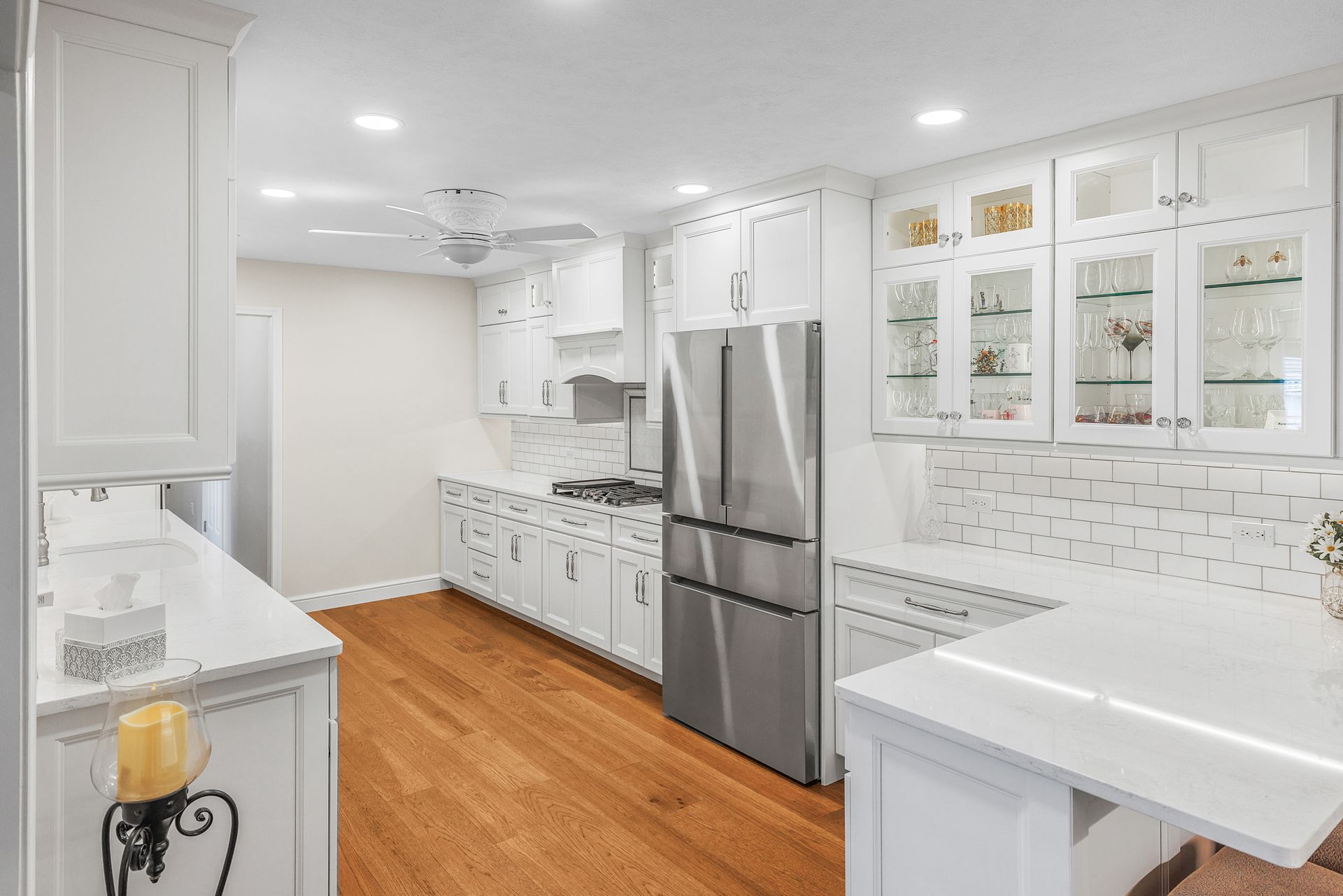 White kitchen with wood floor, stainless steel refrigerator, and glass-door cabinets.