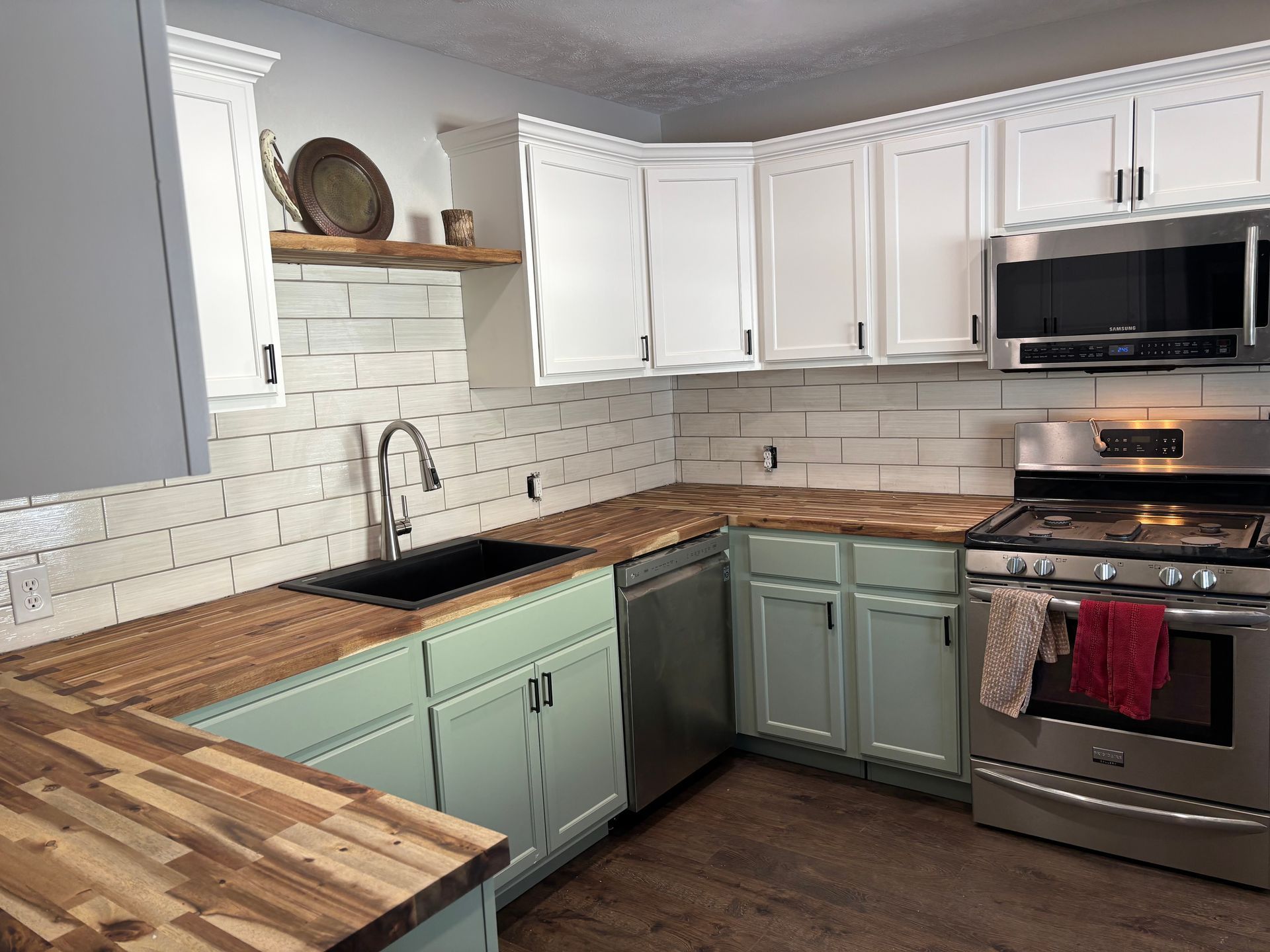 Kitchen with white cabinets, aqua base cabinets, butcher block countertops, stainless steel appliances, and white subway tile backsplash.