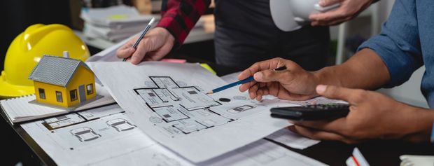 People reviewing blueprints with a model house, hard hat, and calculator.