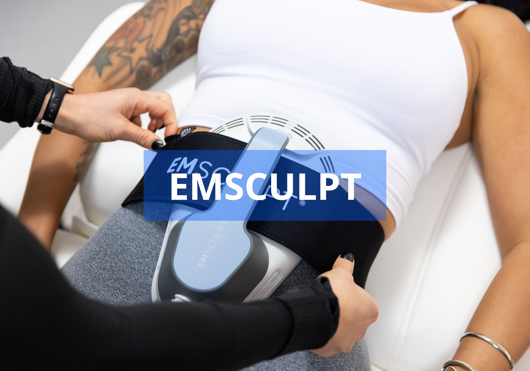 A person receiving an EMSCULPT treatment on their abdomen.  A technician is adjusting the device.