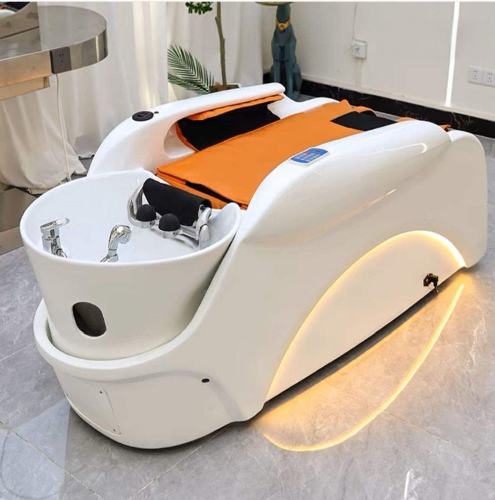 White, modern pedicure spa chair with orange cushion and foot bath basin. Features chrome faucets and subtle lighting.