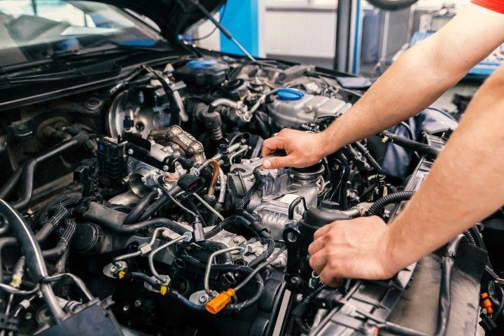 Mechanic working on a car engine in an auto shop, with tools and exposed wiring visible