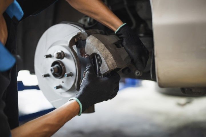 Mechanic wearing black gloves installing a brake disc on a car wheel hub