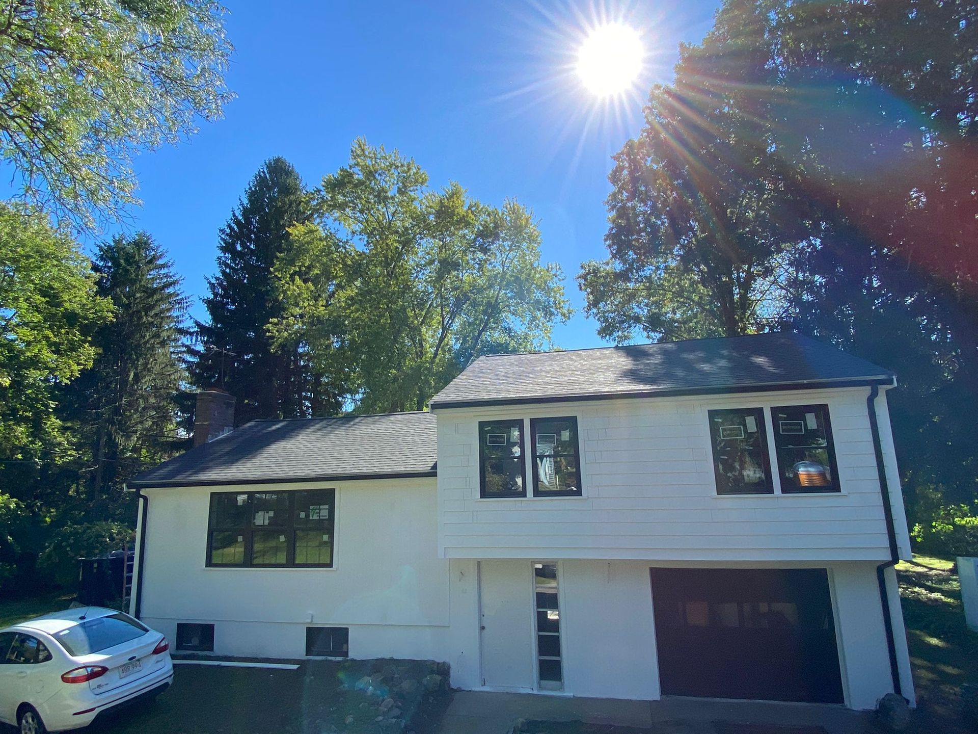 A white house with a car parked in front of it on a sunny day.