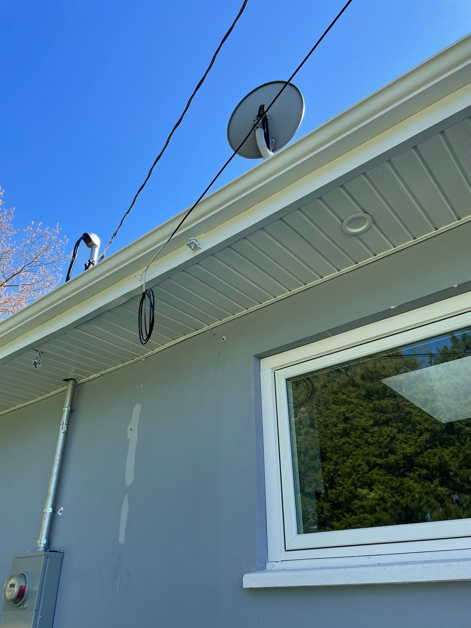 A satellite dish is hanging from the roof of a house