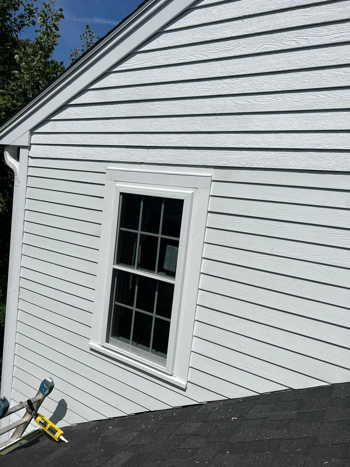 A white house with a window and a ladder on the roof.