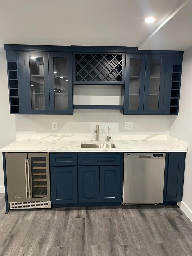 A kitchen with blue cabinets , a sink , a dishwasher , and a wine cooler.