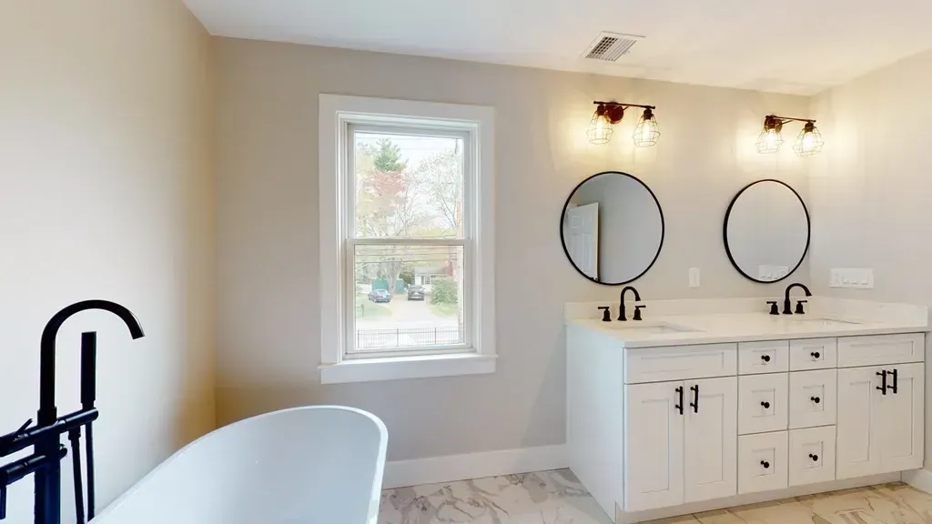 A bathroom with two sinks , a tub , and a window.