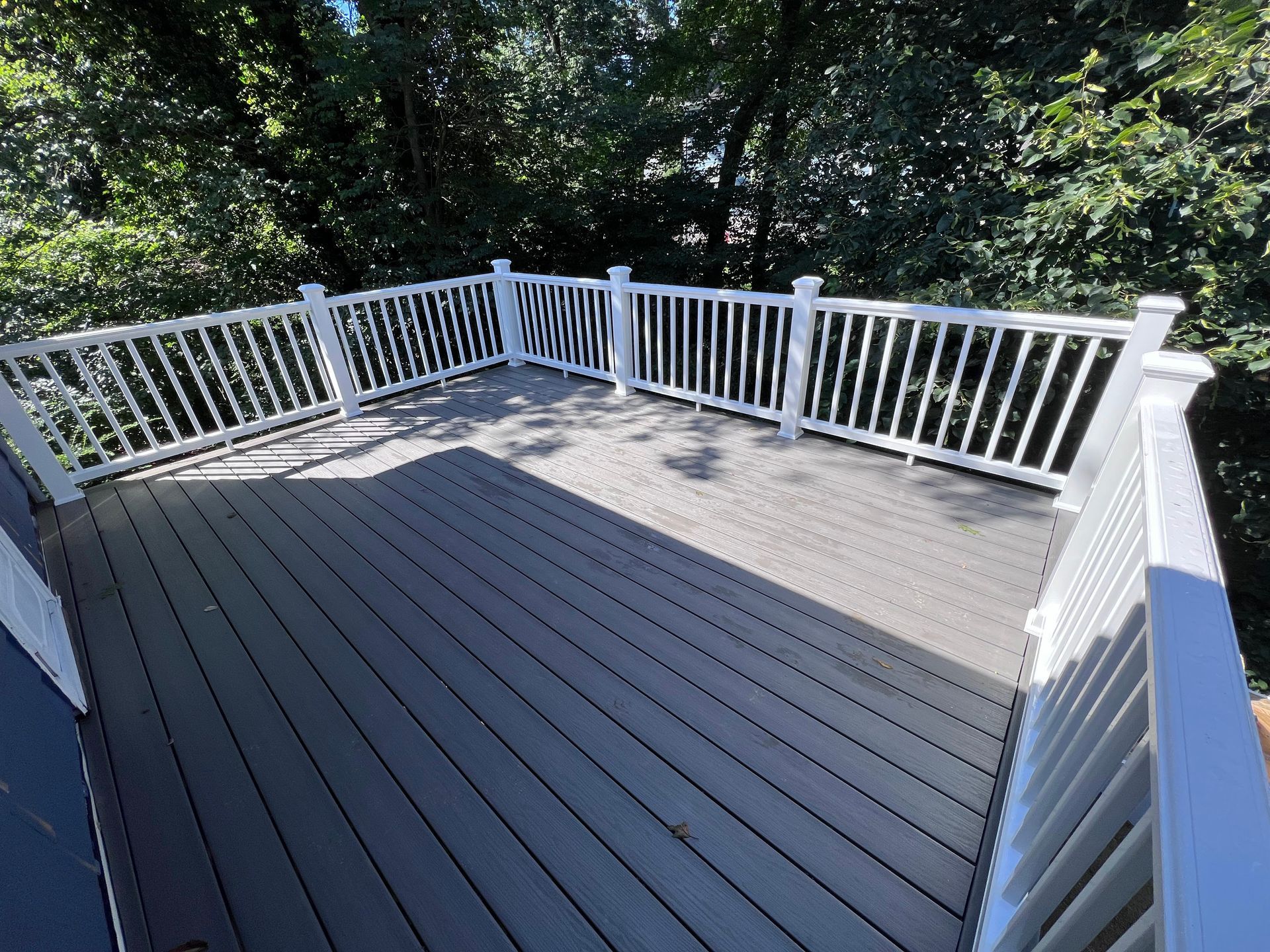 A large deck with a white railing and trees in the background.