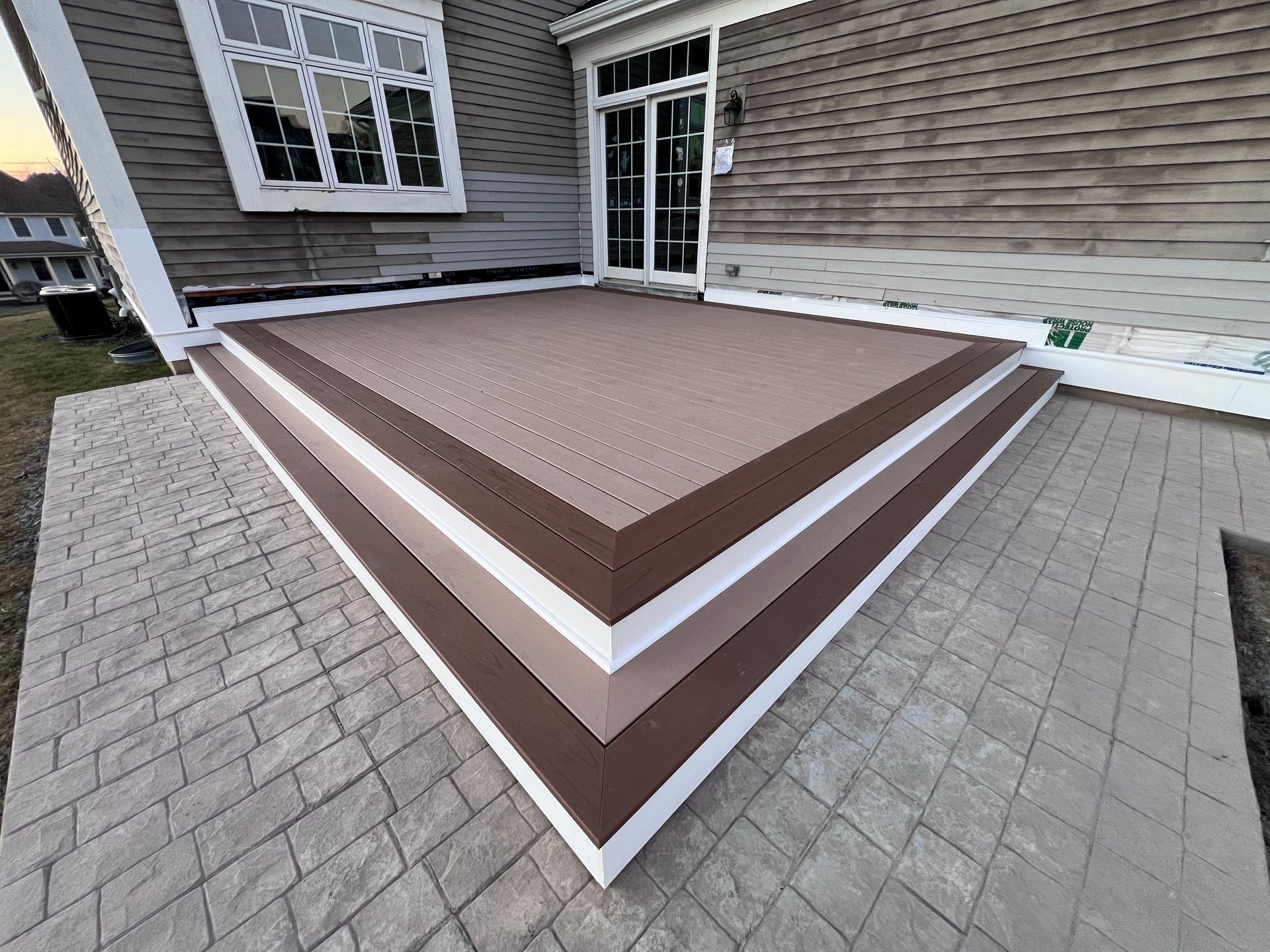 A patio with a brown and white border is in front of a house.