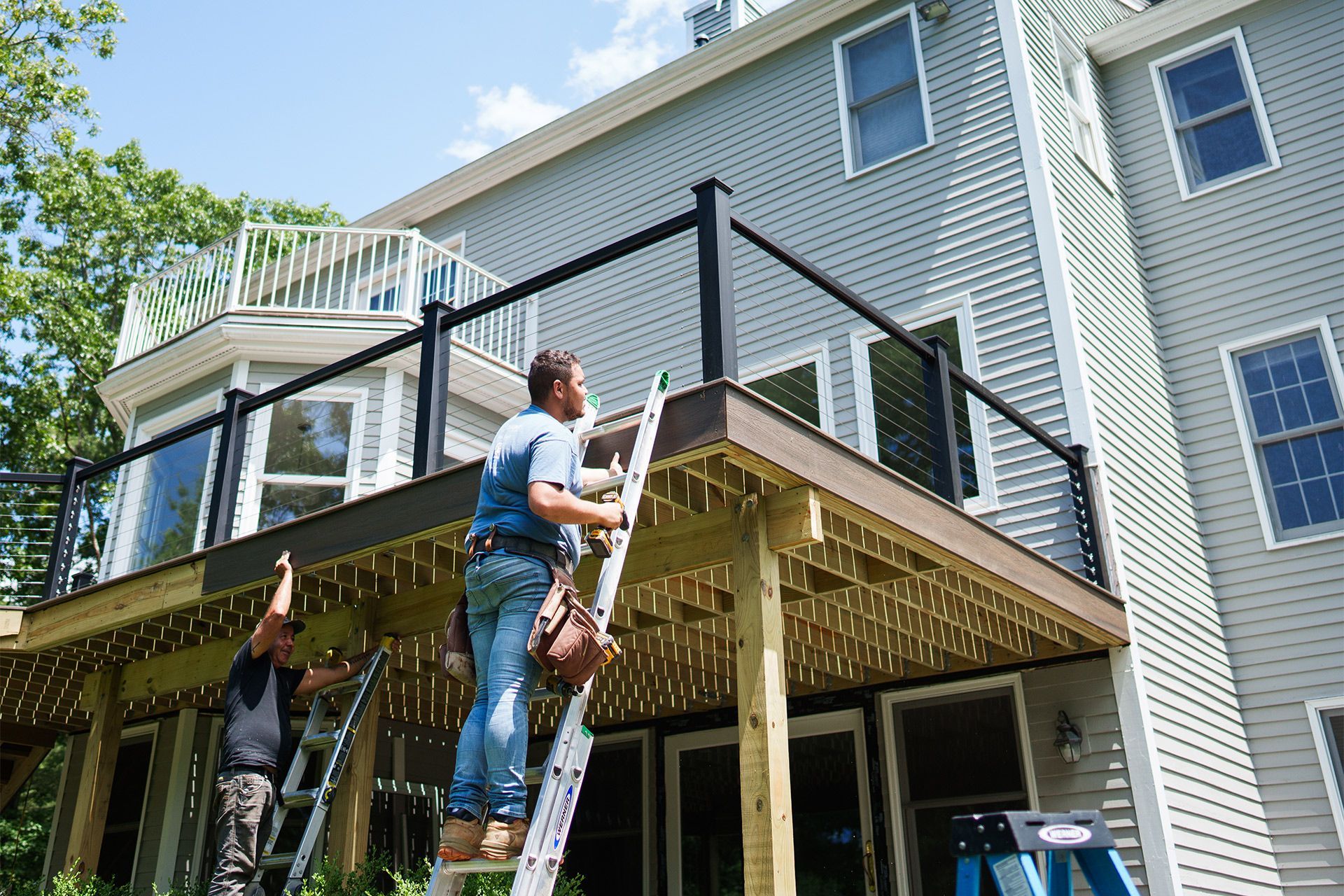 Two men are working on a deck in front of a house.