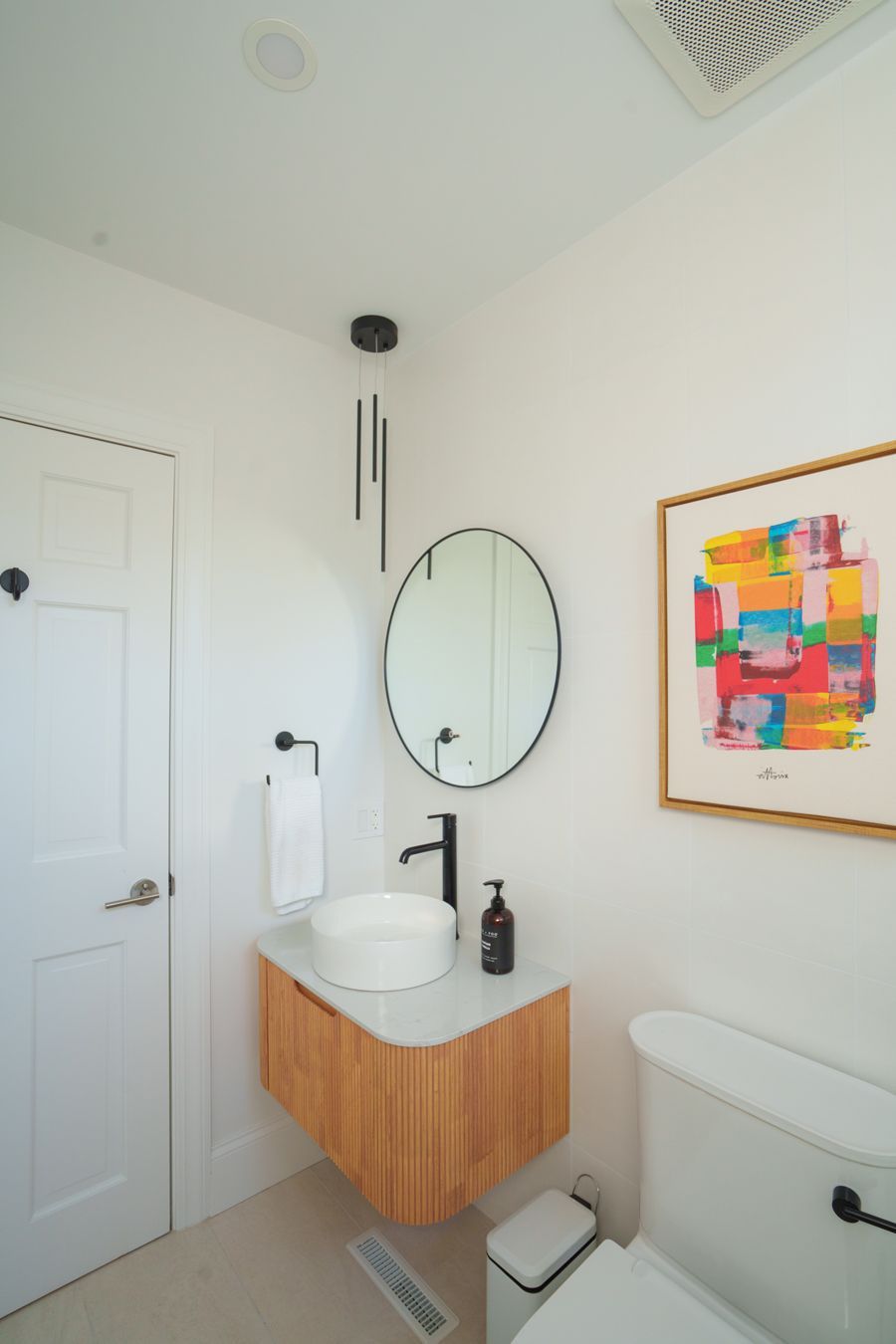 A bathroom with a sink , toilet , mirror and painting on the wall.