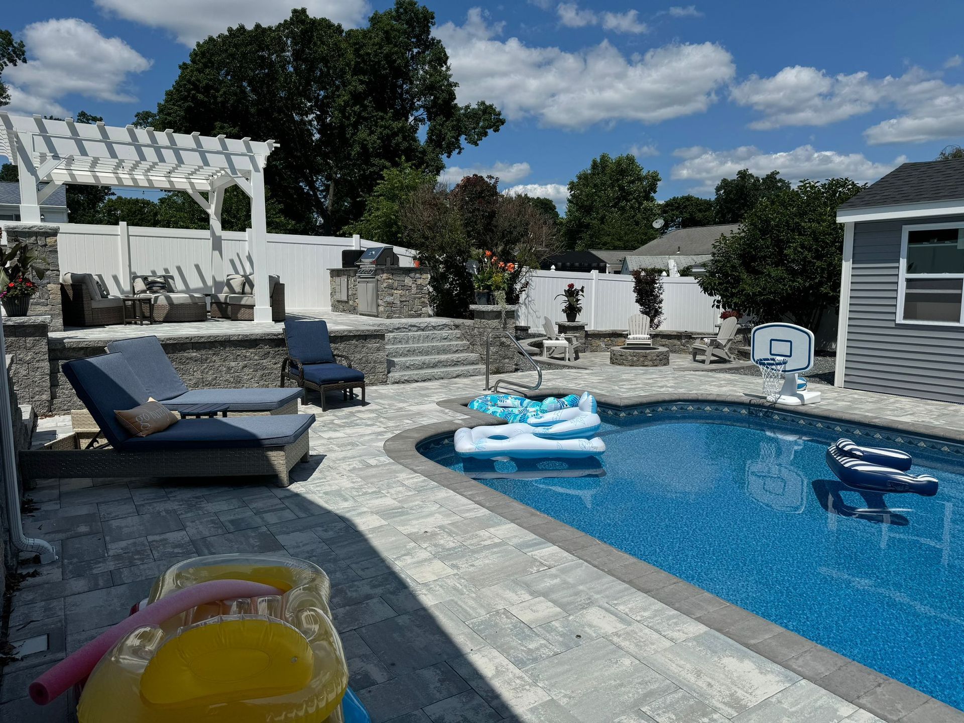 A large swimming pool is surrounded by chairs and a pergola.