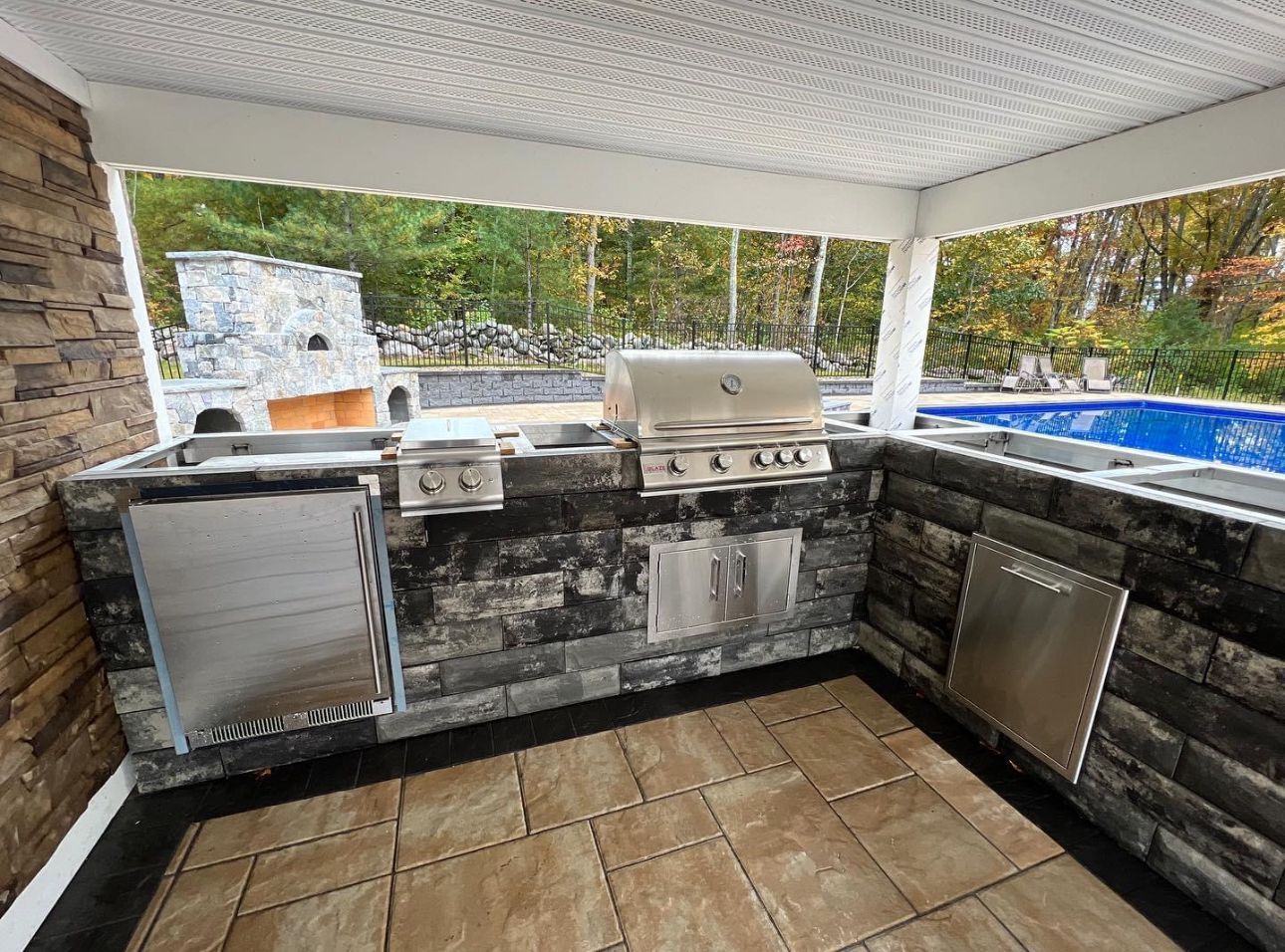 An outdoor kitchen with a grill , sink , and fireplace.