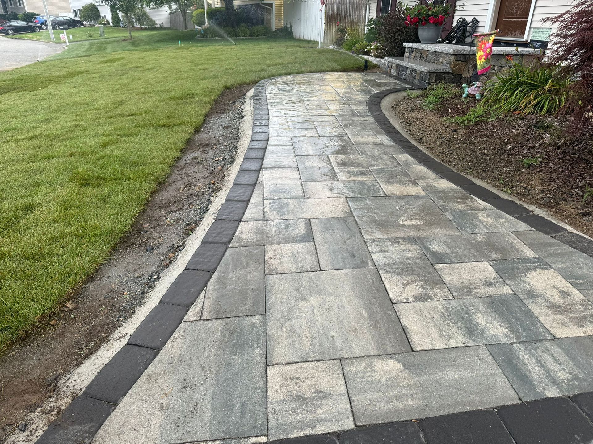A brick walkway leading to a house with a lawn in the background.