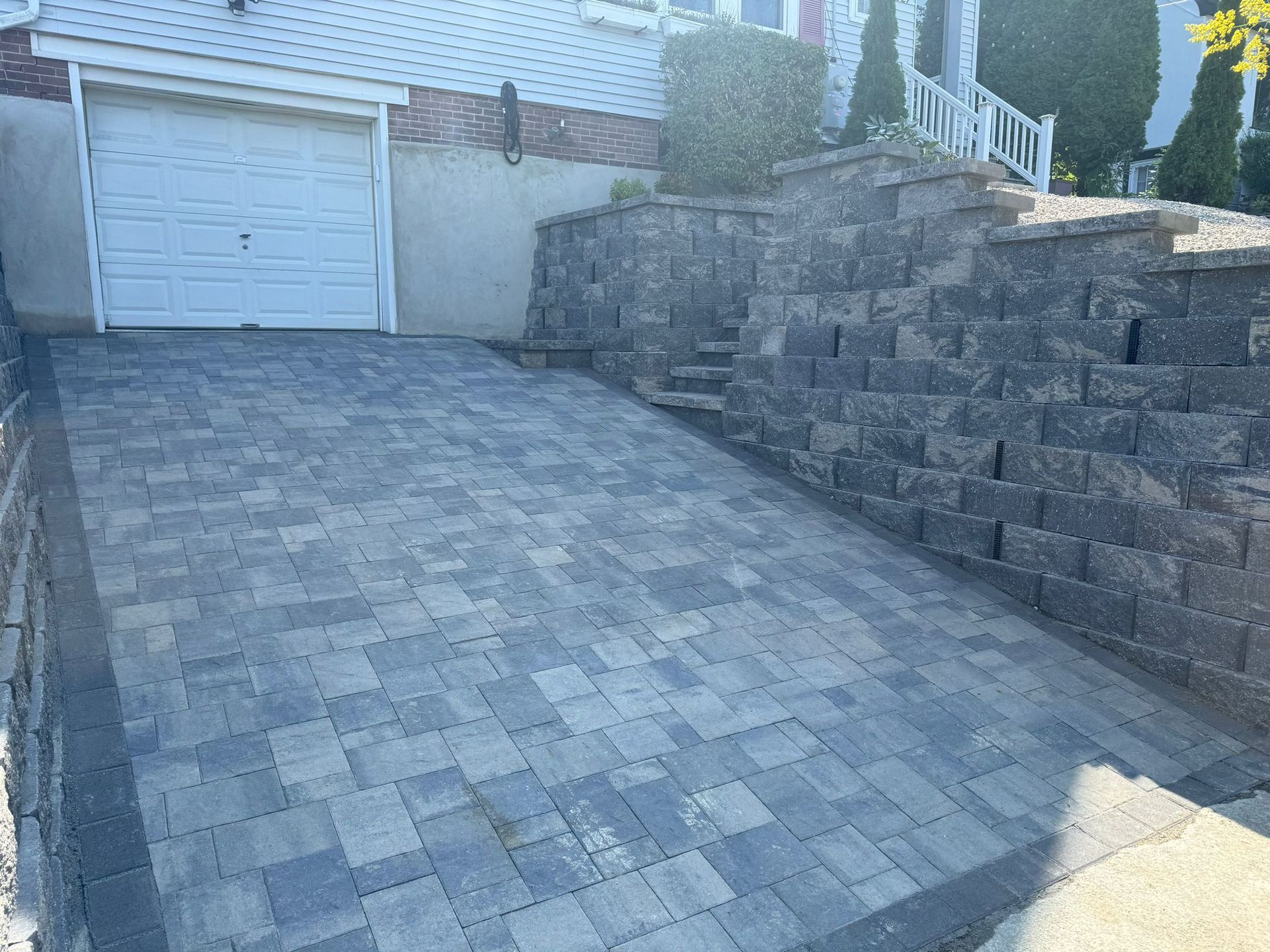 A brick driveway leading to a garage next to a stone wall.