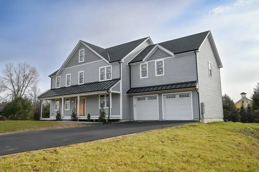 A large house with three garage doors is sitting on top of a grassy hill.