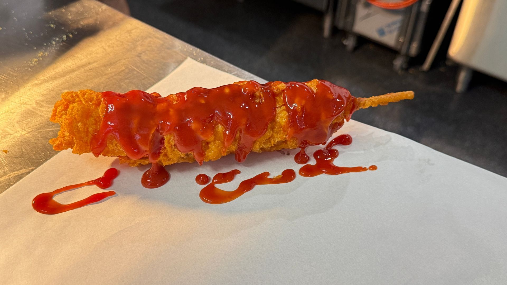 Corn dog with ketchup on a white surface in a kitchen setting.