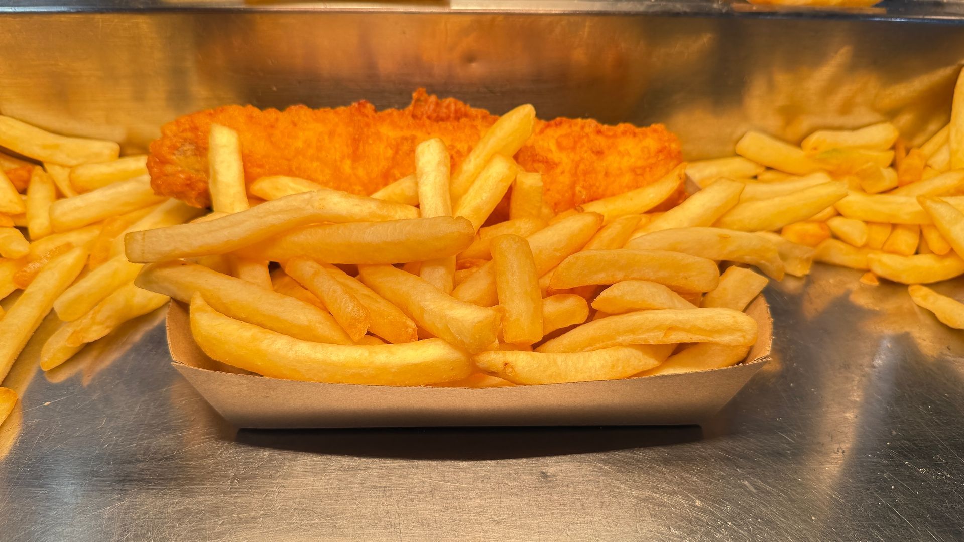 Fish and chips, fried golden with a fillet of fish nestled in a container of fries.