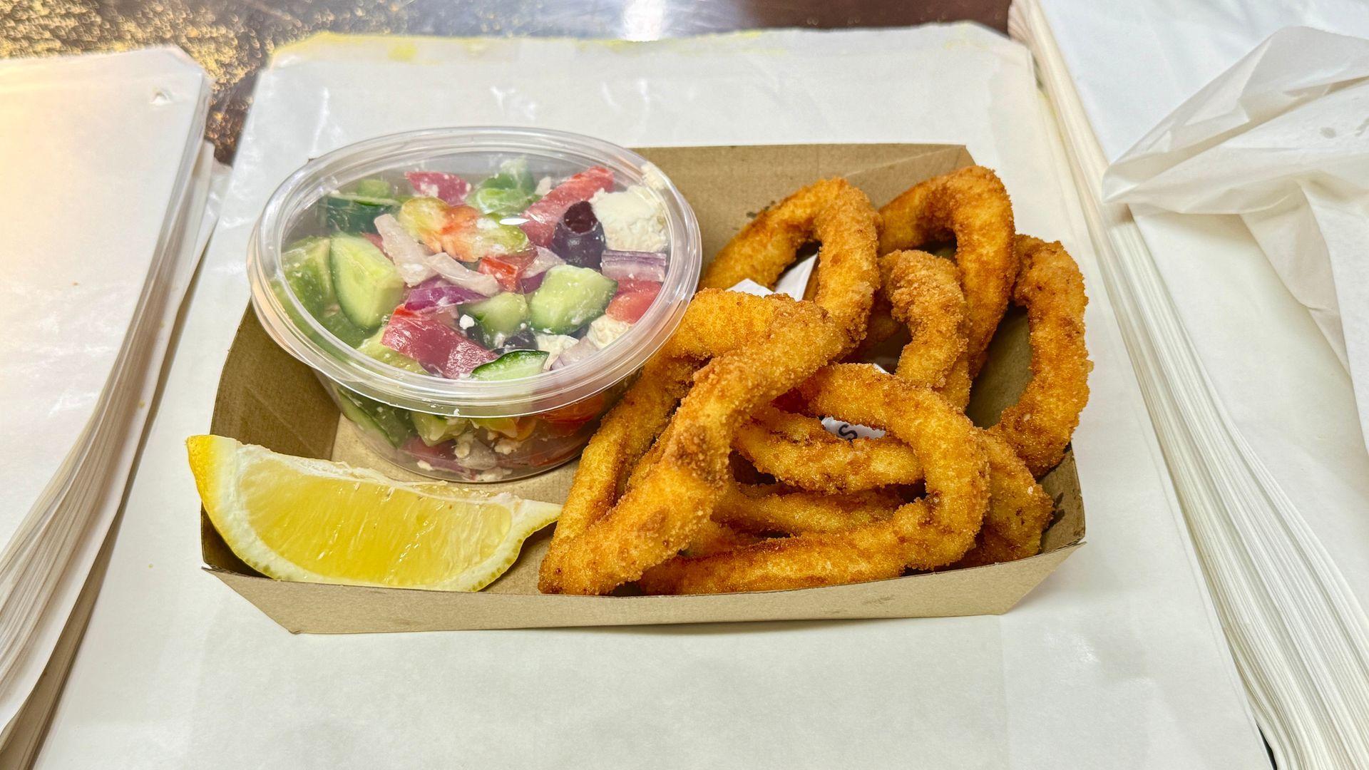 Calamari rings, salad, and lemon wedge in a cardboard container.