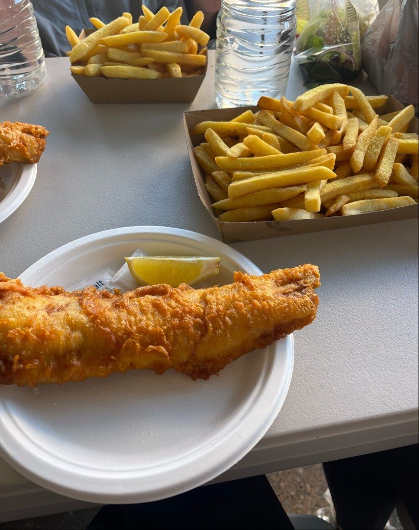 Fried Fish and Fries on a Table, With a Lemon Wedge and Water Bottles — Aussie Fish & Chips Nelson Bay in Nelson Bay, NSW