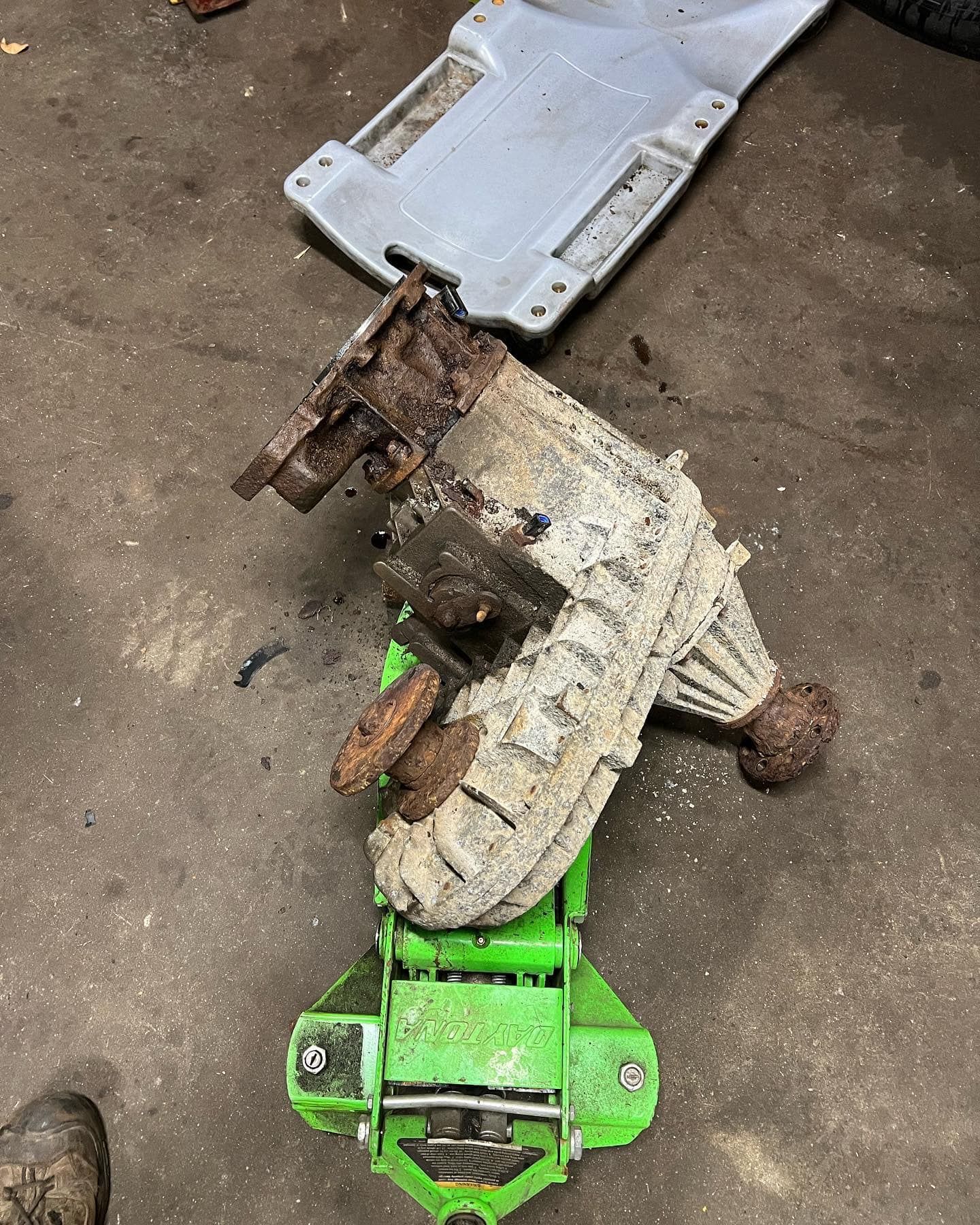 Rusty car part on a green jack; a white plastic creeper is in the background on a concrete floor.