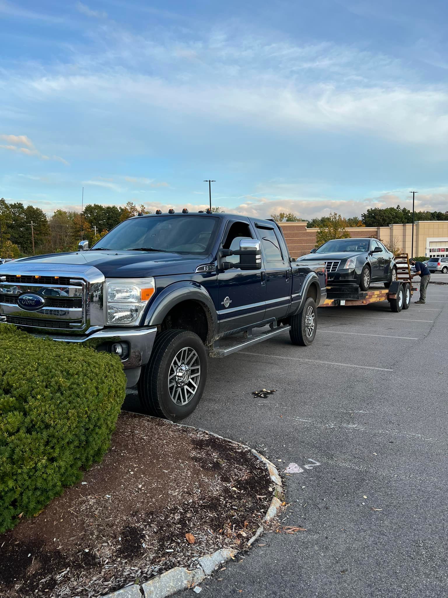 Dark blue Ford truck towing a car on a trailer in a parking lot.
