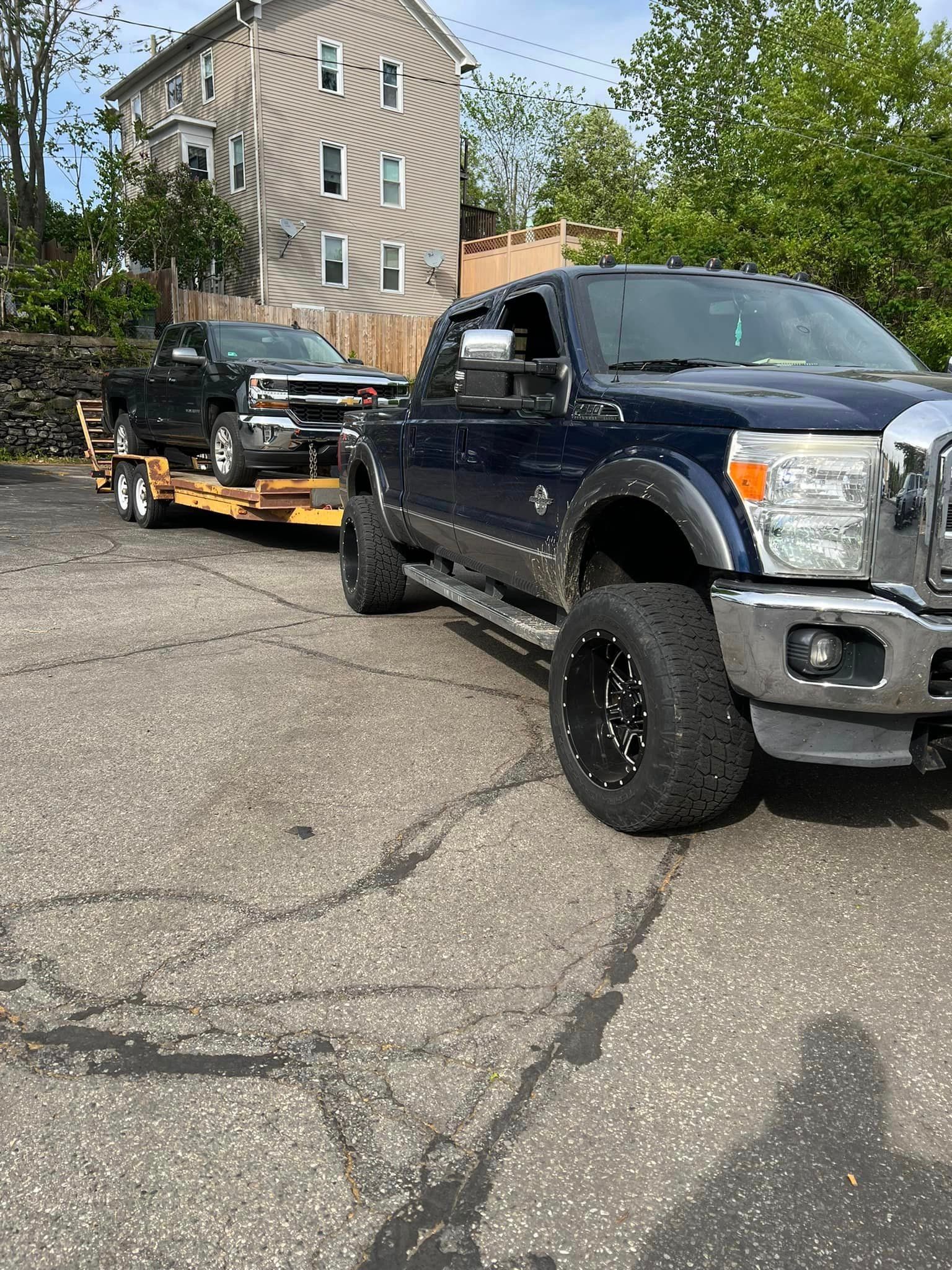 A dark blue pickup truck towing a car on a trailer in a parking lot.