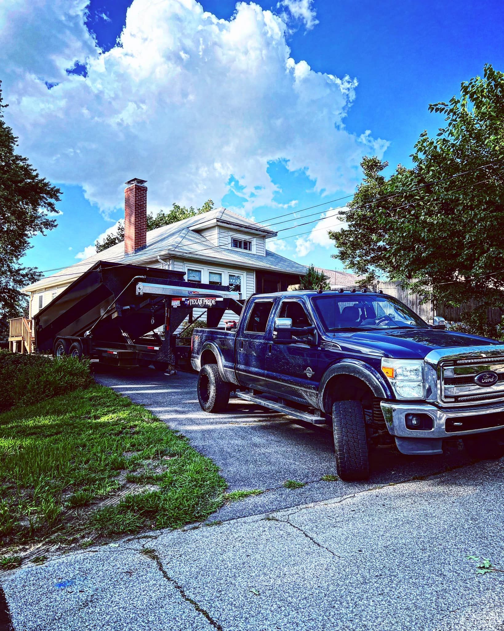 Blue pickup truck towing a trailer on a driveway in front of a house on a sunny day.