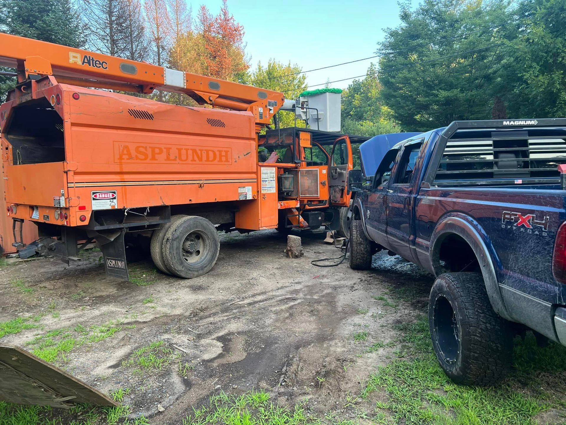 Orange tree chipper next to a blue pickup truck. Both are parked on dirt.