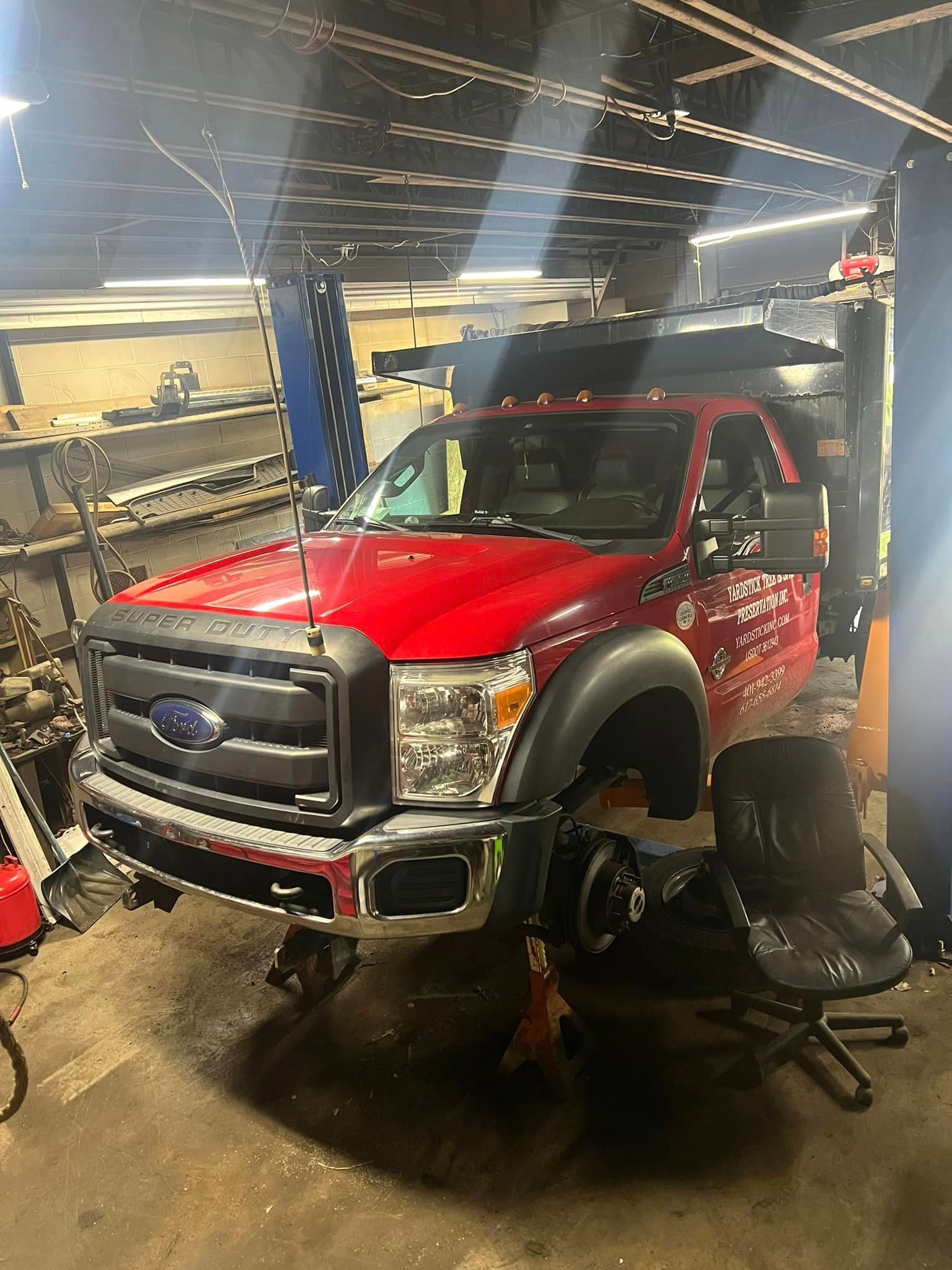 Red Ford truck on a lift in a garage, wheels removed, under repair.