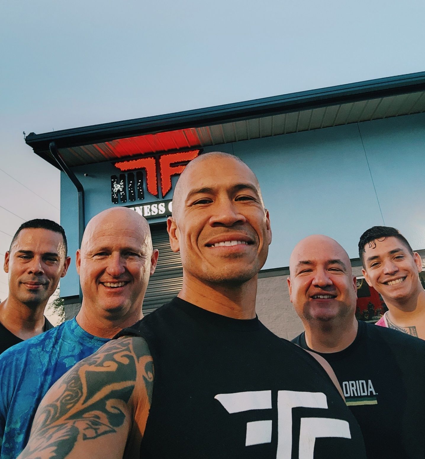 A group of men are posing for a picture in front of a building that says tf