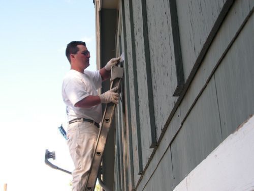 A man is standing on a ladder painting a building