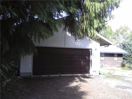 A garage with a brown door is surrounded by trees