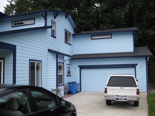 A white truck is parked in front of a blue house