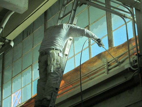 A man is standing on a ladder painting a building.