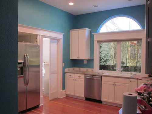 A kitchen with blue walls and white cabinets and a stainless steel refrigerator