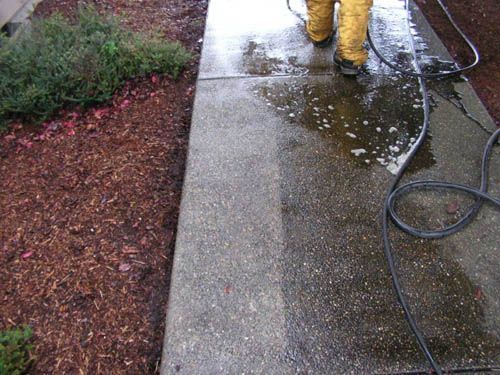 A person is cleaning a sidewalk with a pressure washer.