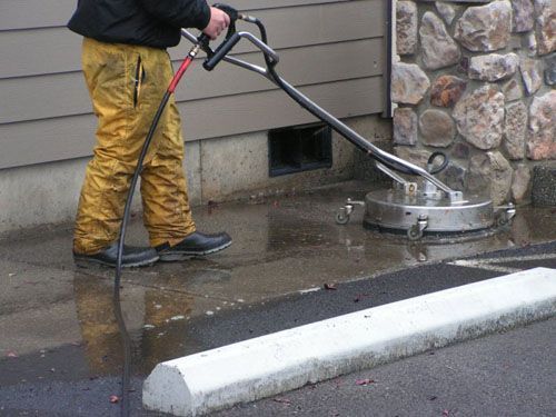 A man is using a high pressure washer to clean a sidewalk