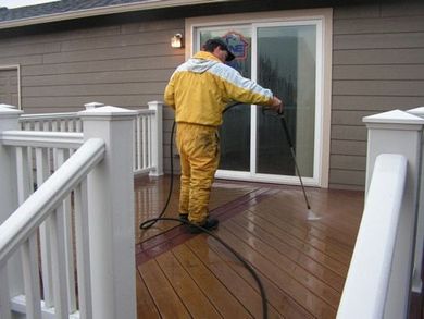 A man is cleaning a deck with a high pressure washer