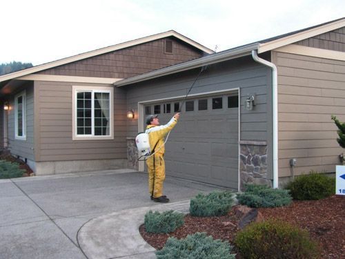 A man spraying a garage door with a sprayer in front of a house