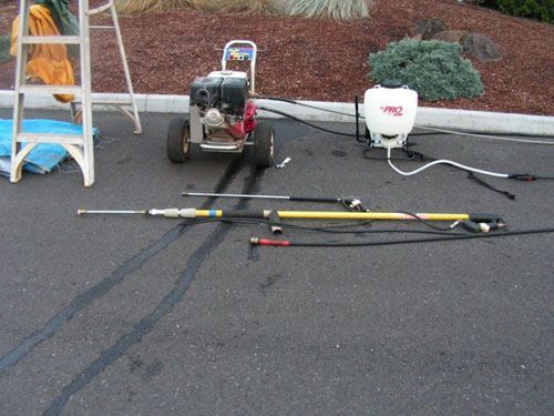 A lawn mower is parked next to a sprayer and a ladder