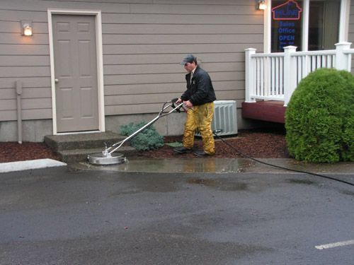 A man is cleaning the sidewalk in front of a house with a machine.