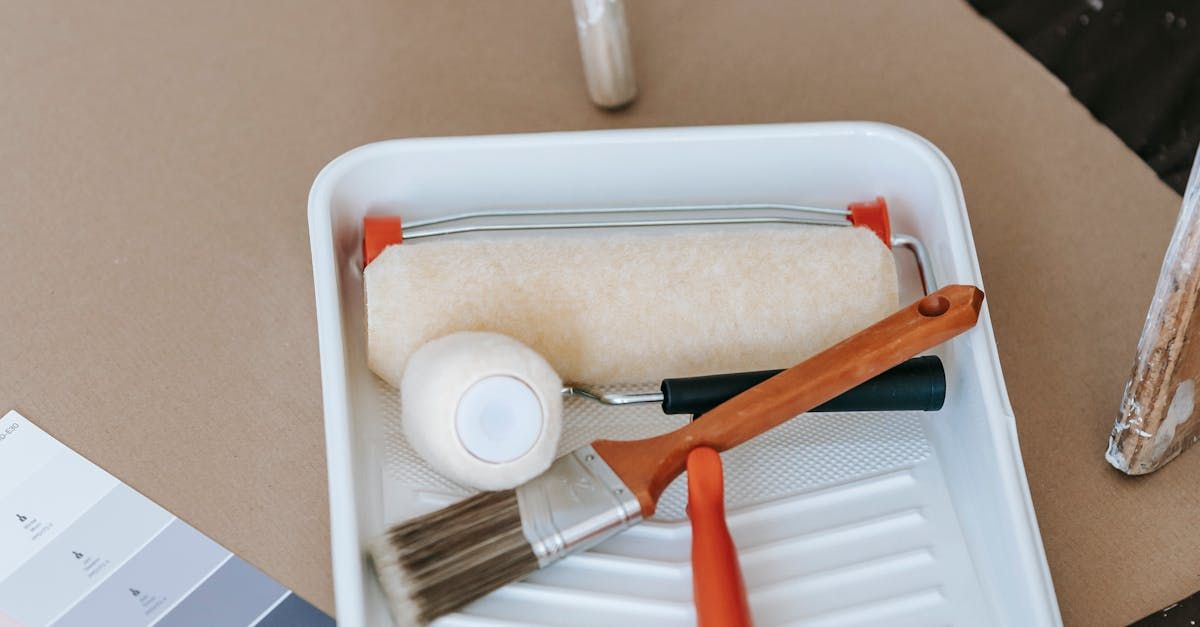 A paint tray filled with paint rollers , brushes , and a spatula.