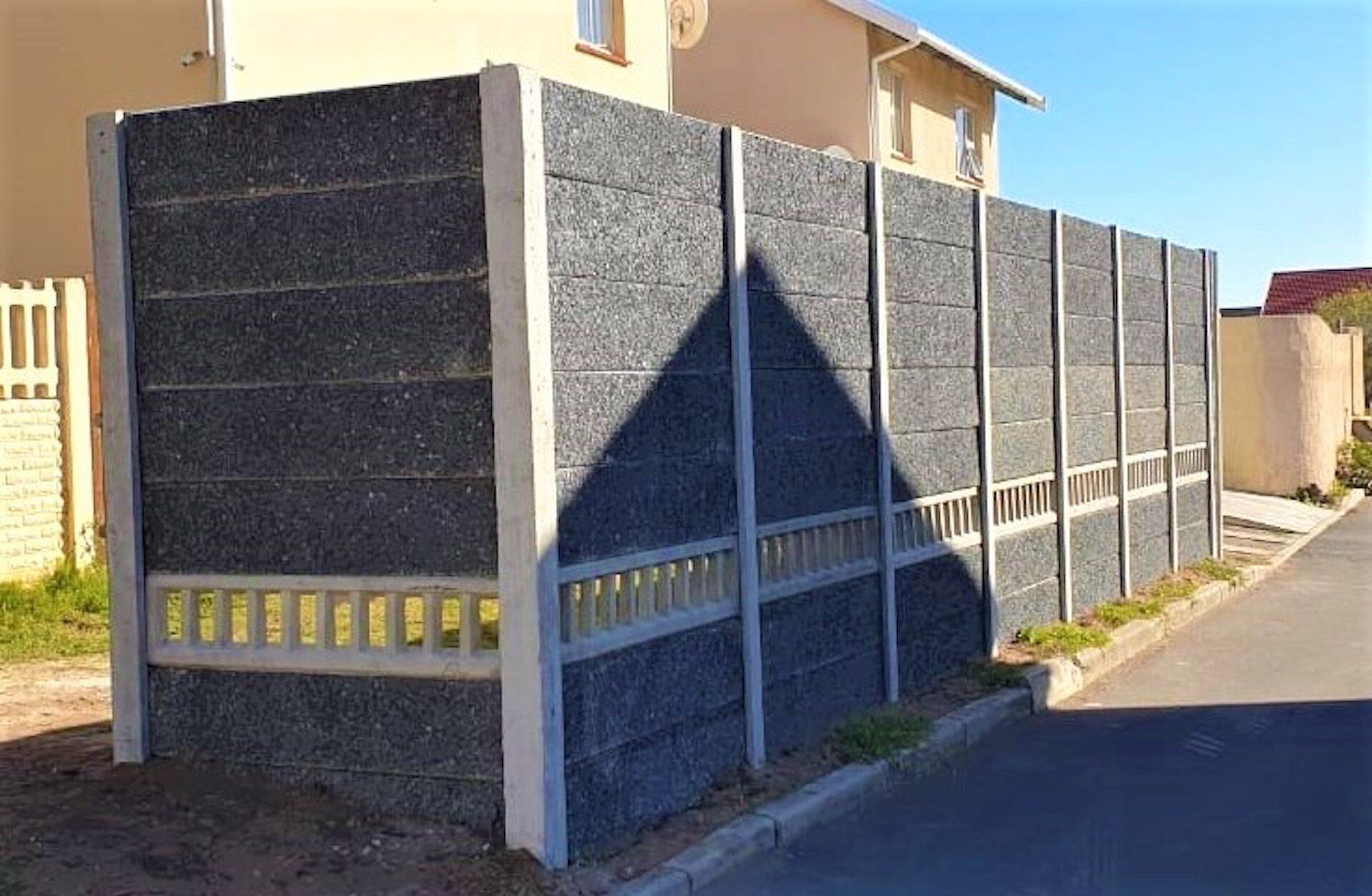 A concrete fence is sitting on the side of the road next to a house.